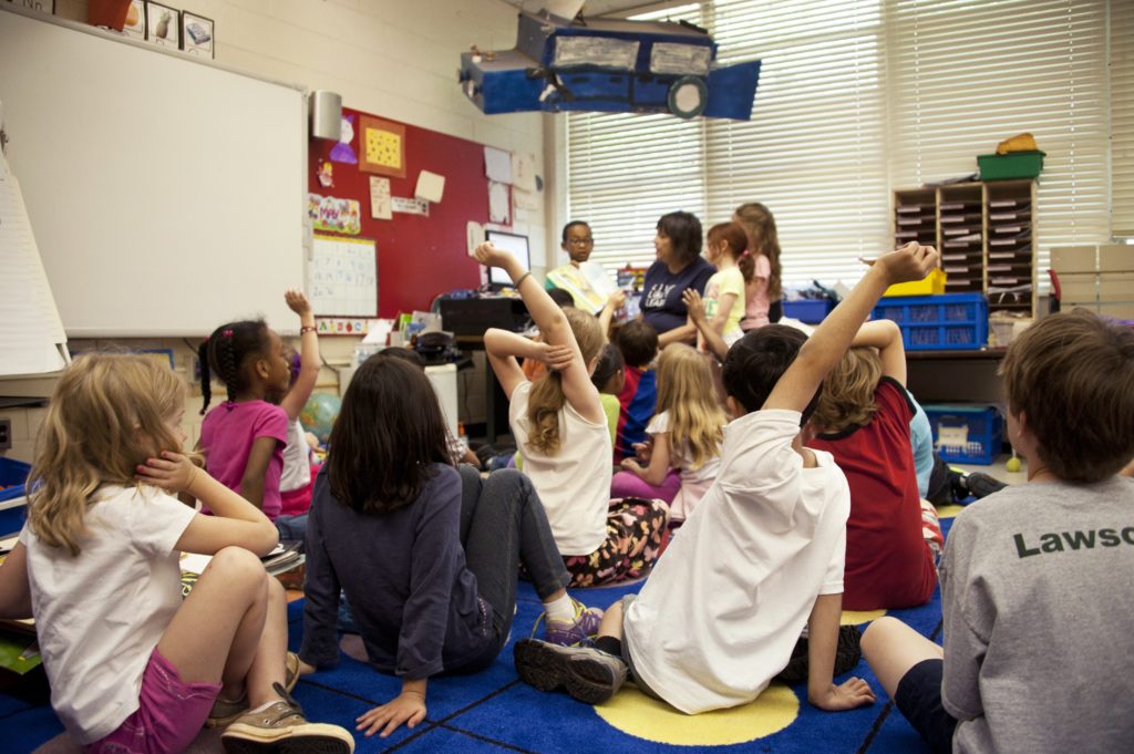 des enfants assis par terre sur des tapis en classe